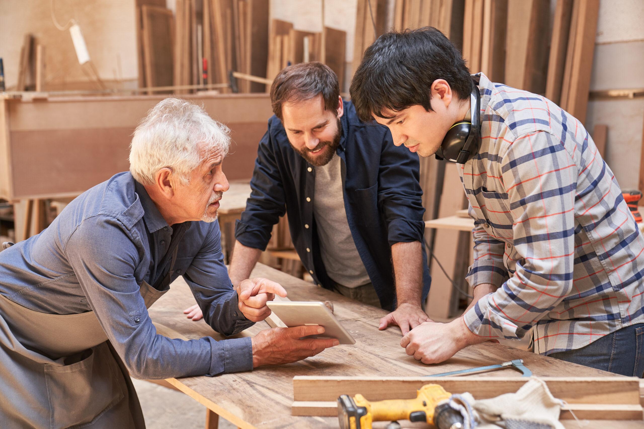 Artisan senior expliquant le travail à la relève dans un atelier - Transmission d'entreprise