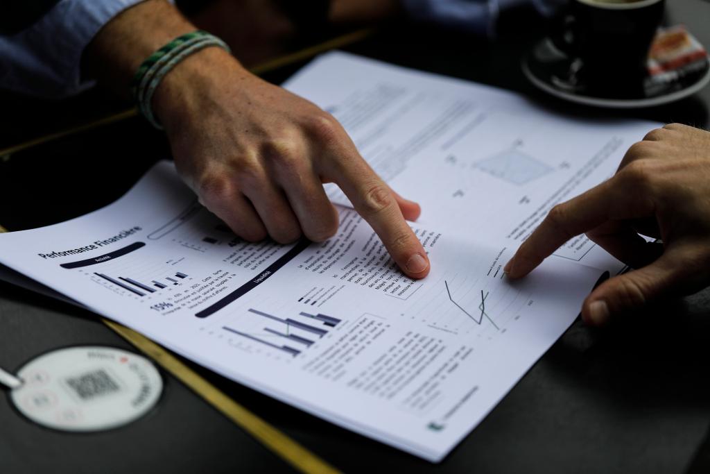 Photo de documents d'analyse de la performance financière d'une entreprise avec une main pointant certains élements